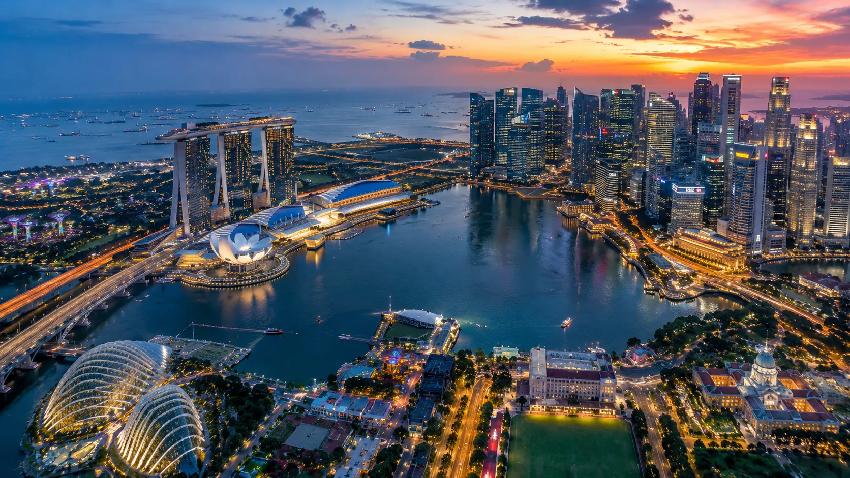 An aerial view of Singapore's Marina Bay at dusk, with the skyline lit up across the water